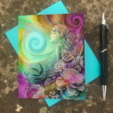 Greeting card featuring artwork of a flourish of colorful flowers surrounding a youthful goddess called Flower Child by Primal Painter with a blue envelope