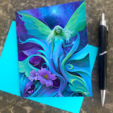 Greeting card featuring artwork by Primal Painter of an ethereal fairy amidst swirling art nouveau flowers and foliage in greens, purples, and blue with a blue envelope